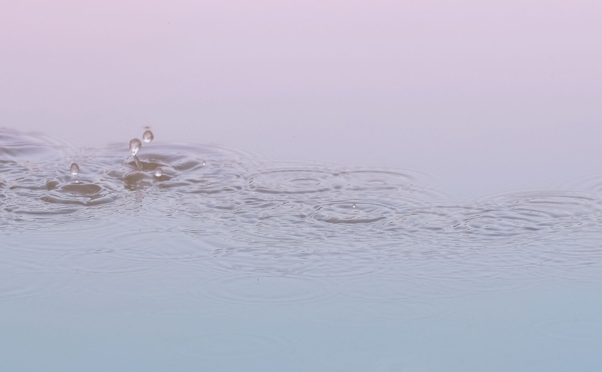 Wassertropfen fallen auf eine Wasseroberfläche und ziehen Kreise.