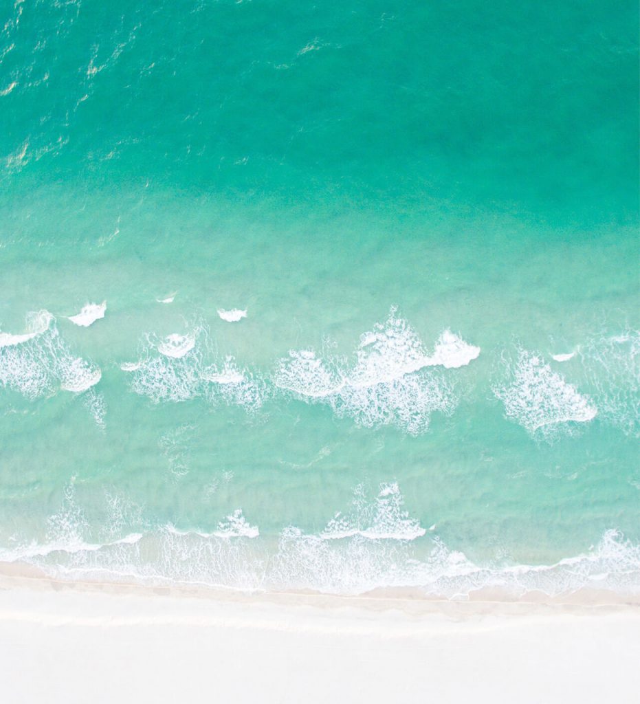 Aufnahme von einer Drohne von Wellen, die sich am Strand brechen.