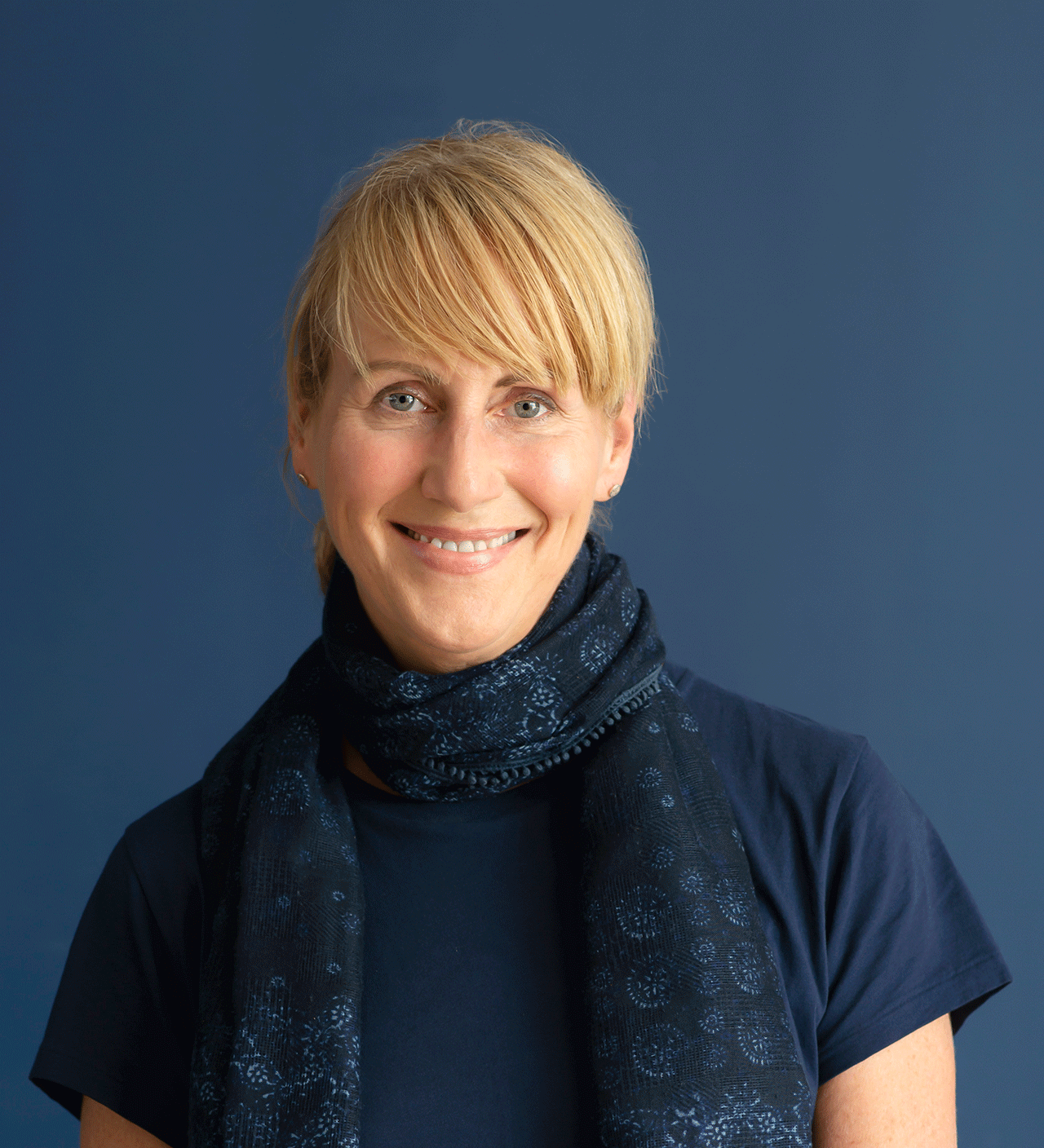 Eine lächelnde blonde Frau trägt einen blauen Schal.