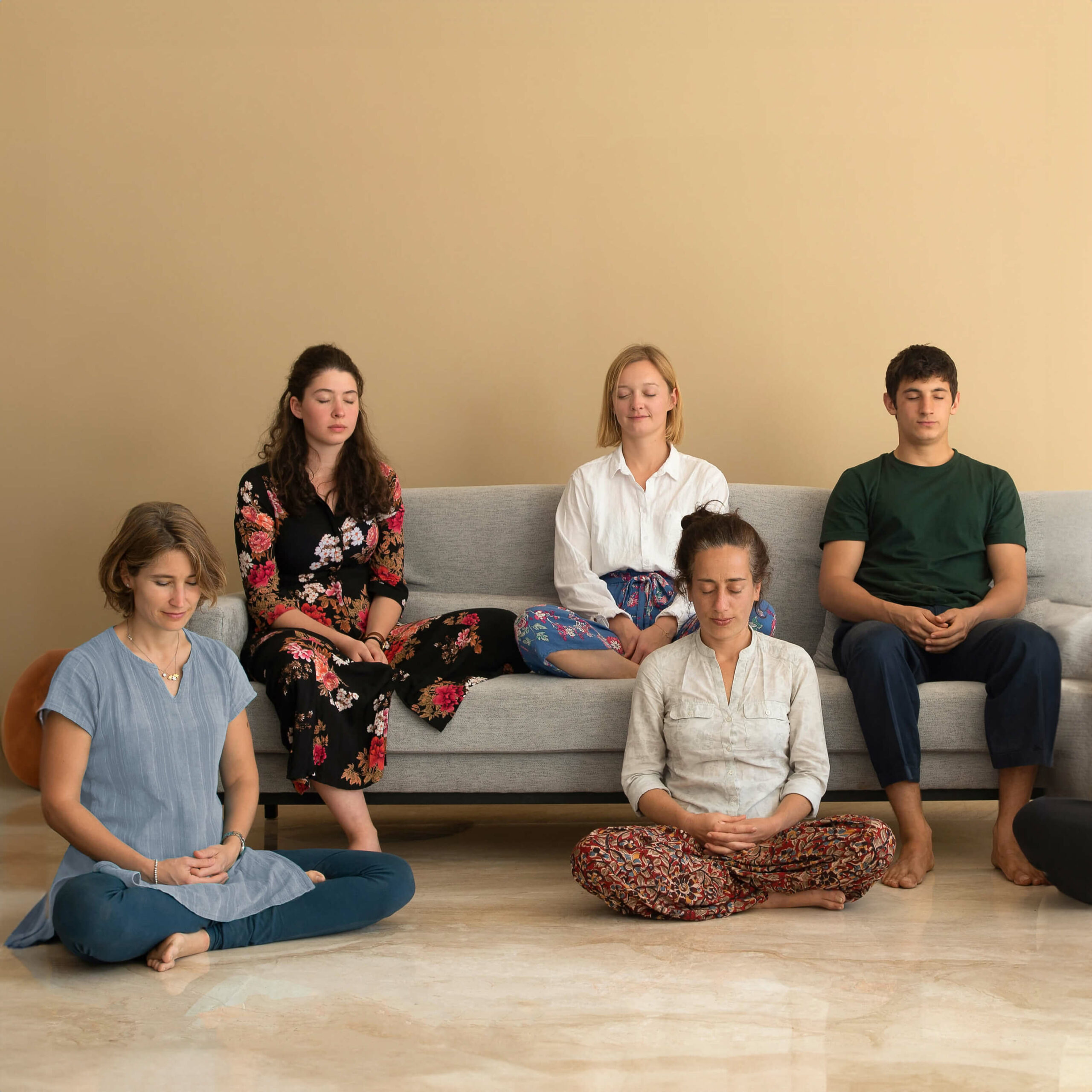 Fünf junge Menschen meditieren zusammen auf dem Sofa.